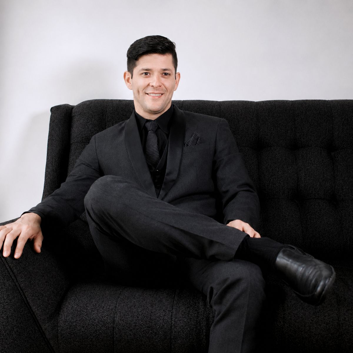 Caballero con traje entero negro sentado relajado en sofá oscuro