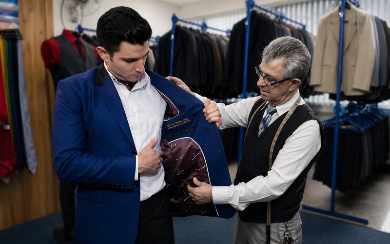 Sastre ajustando un saco azul a un cliente en el local de Trajes Eventuales